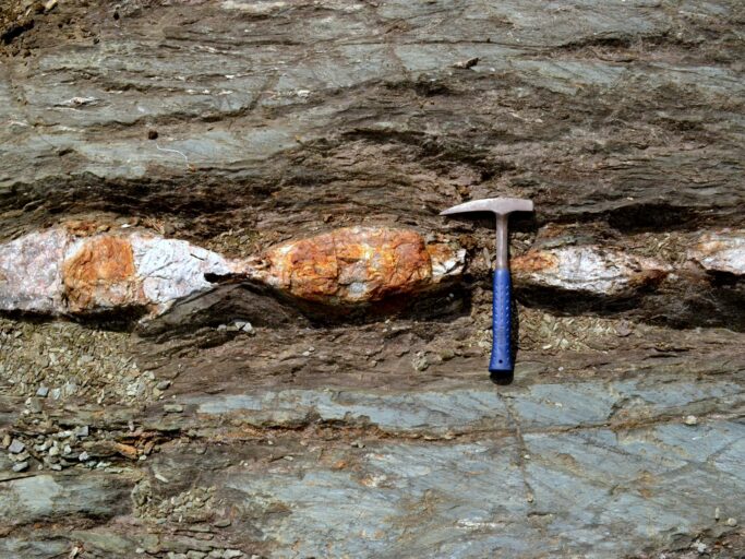 Fault zone - Most ore deposit types formed through fluids that dissolved and re-precipitated the metals of interest. These fluids find pathways to travel through the Earth’s crust, for example, in fault zones (i.e. large-scale cracks in the ground). The origin of these fluids just like the origin of the metals, however, are not well-constrained in many cases. This is particularly true for Archean deposits, which were printed several times over the course of billions of years. This photo shows part of the fault zone, containing strongly deformed, stretched, and ripped apart rocks (photo credit: Kamil Bulcewicz)