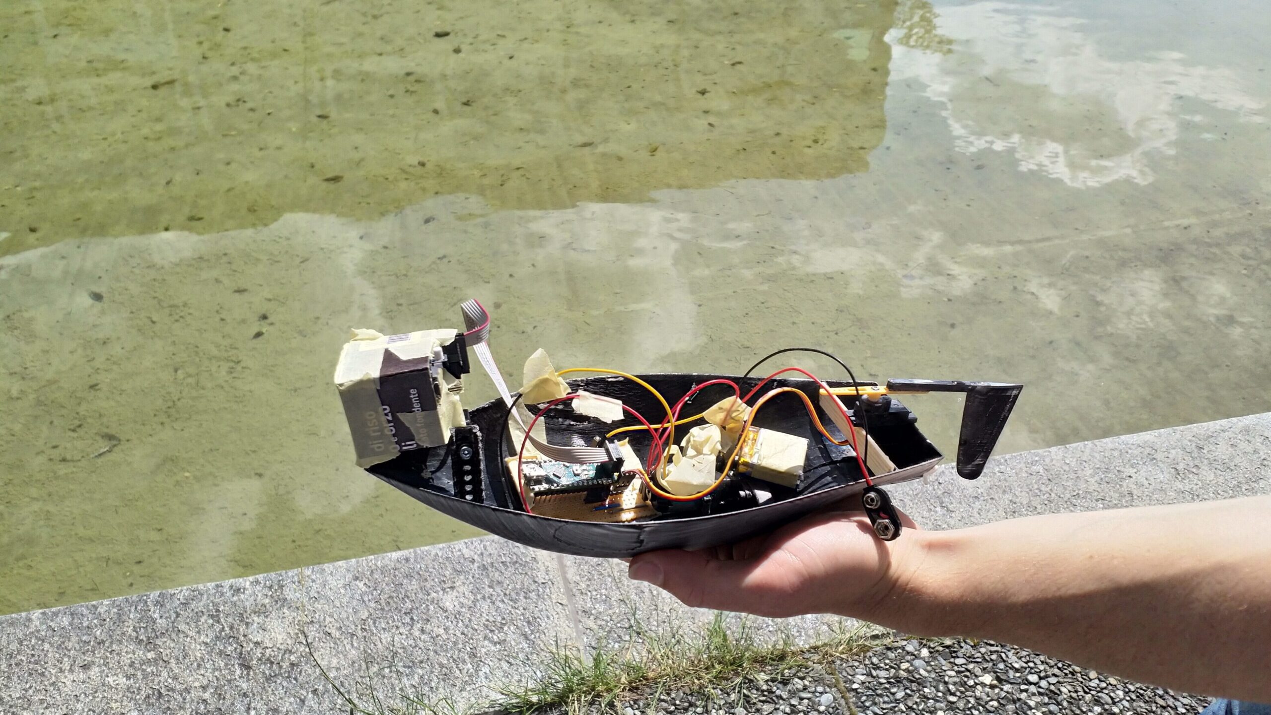 A hand is shown holding a small home-made boat. There are lots of electronic elements visible.